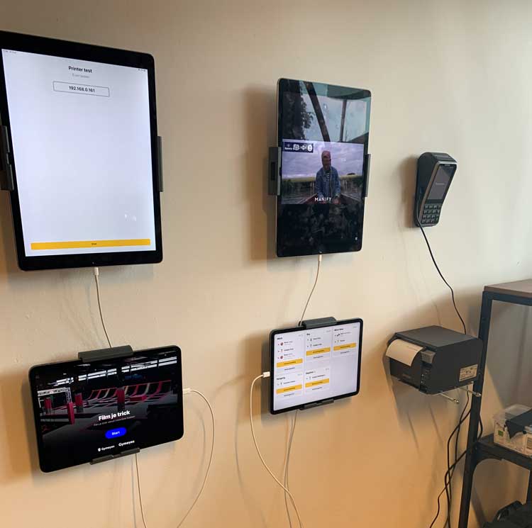 Wall-mounted tablets and a payment terminal connected by cables, alongside a printer with a label roll.